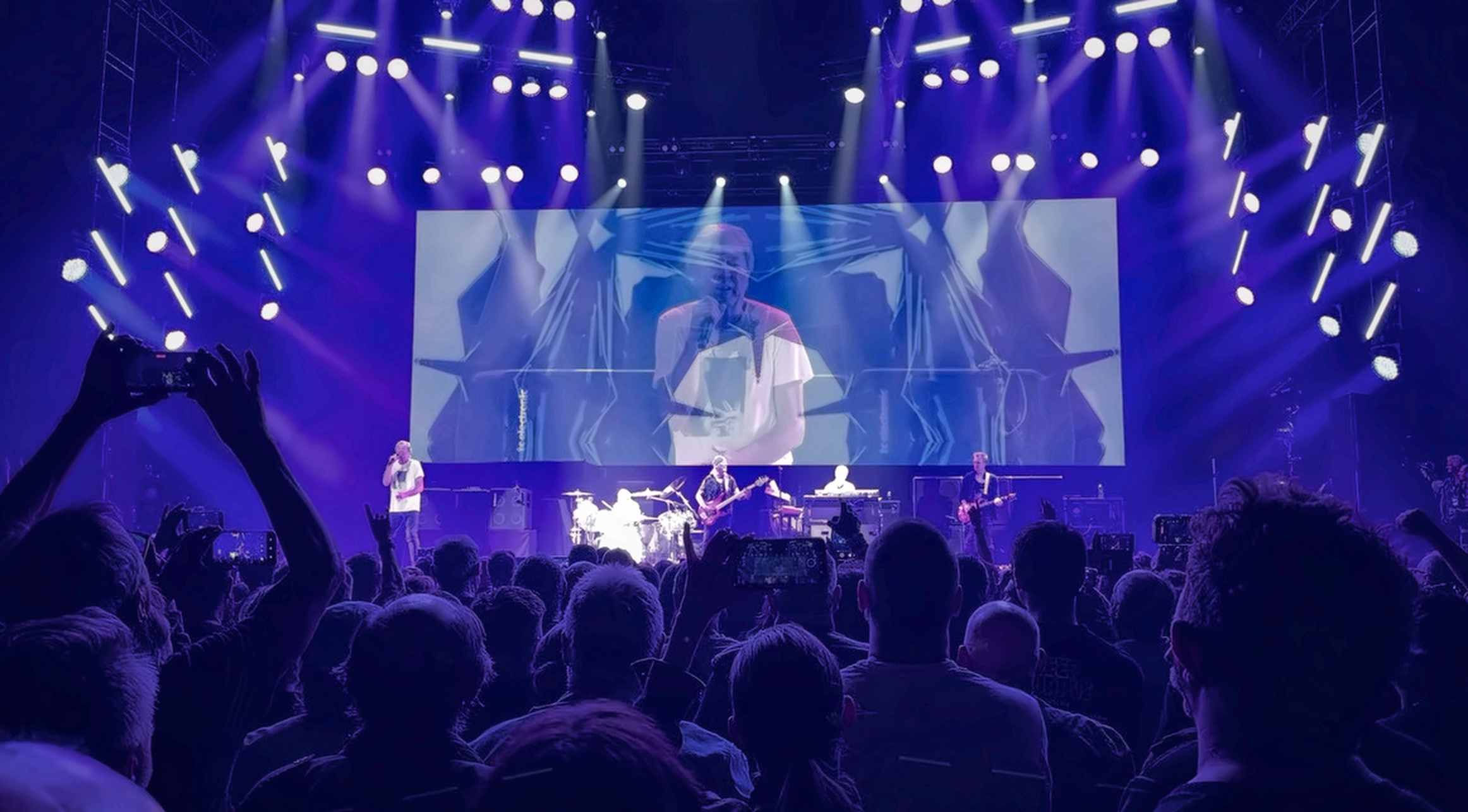 Deep Purple performing on a blue-lit stage, seen from the crowd.